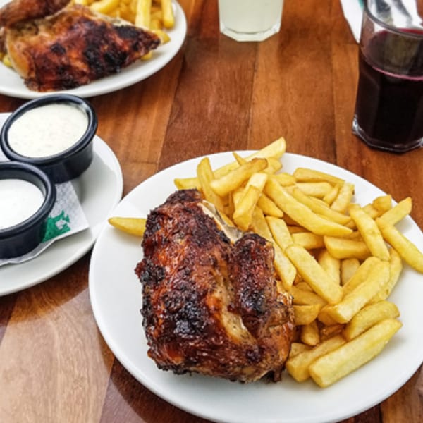 Plates of grilled chicken and french fries, with dipping sauces and drinks on a wooden table.