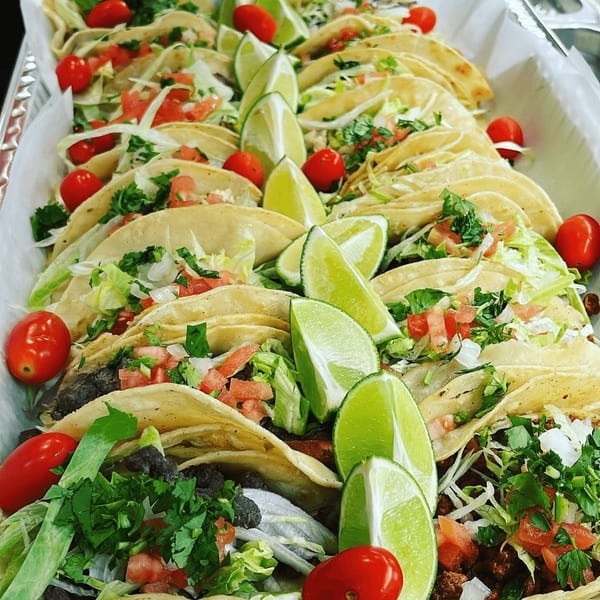 A tray of Speedy Tacos, garnished with fresh lettuce, tomatoes, cilantro, and lime wedges.