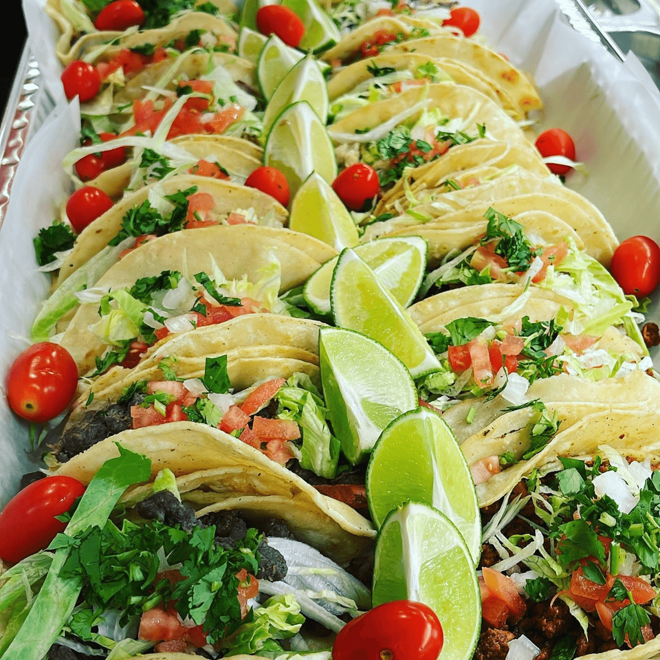 A tray of Speedy Tacos, garnished with fresh lettuce, tomatoes, cilantro, and lime wedges.
