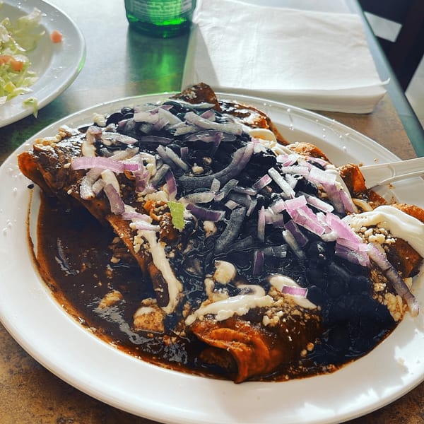 Speedy Tacos and Chicken's enchiladas with dark mole sauce, black beans, red onions, and crema.