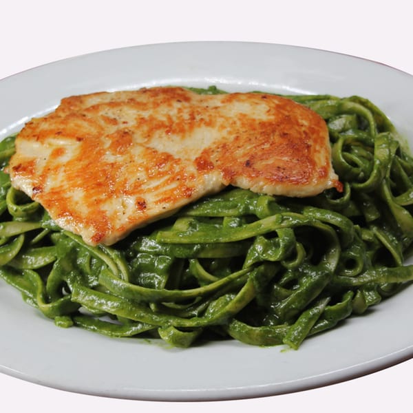 Grilled chicken breast served over a bed of vibrant green pasta on a white plate.