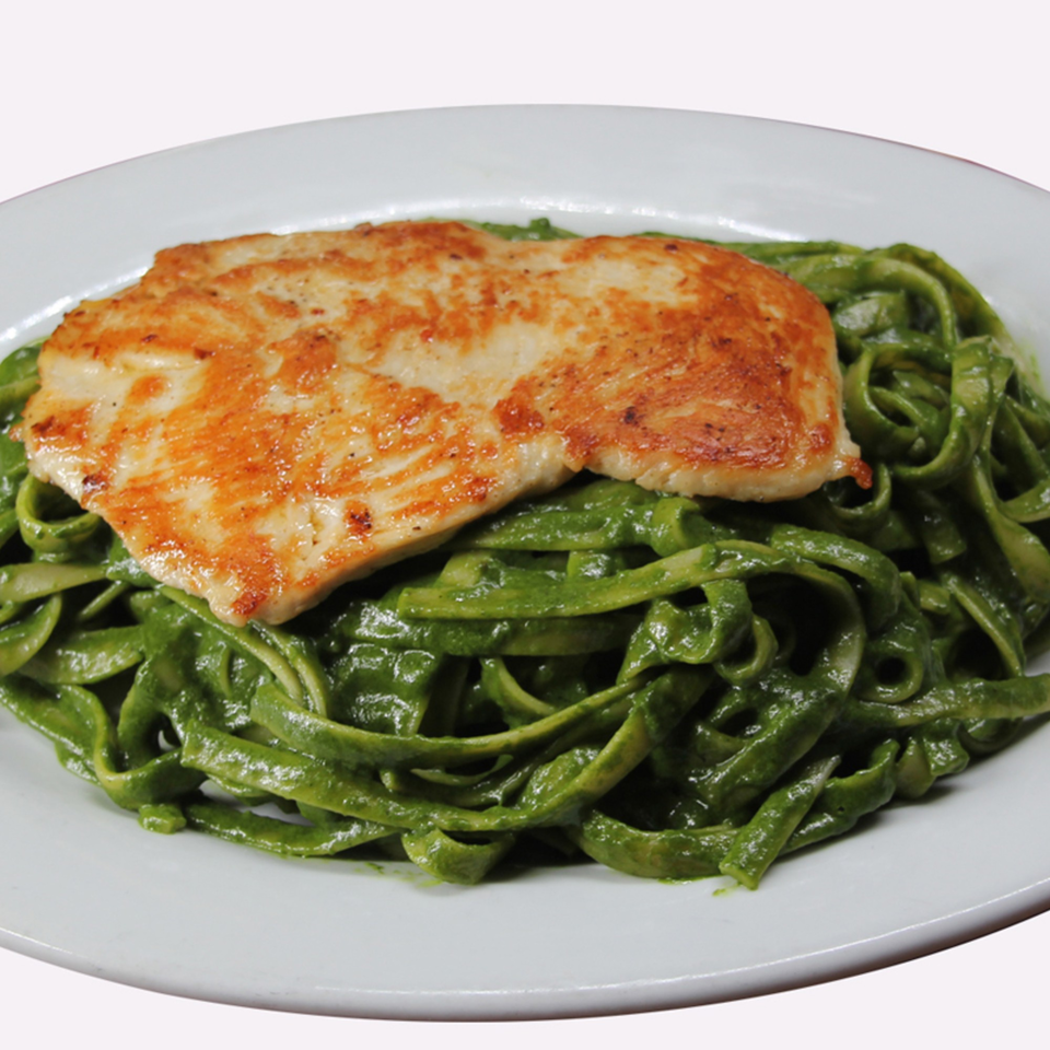 Grilled chicken breast served over a bed of vibrant green pasta on a white plate.
