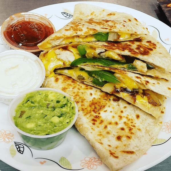 Chicken and cheese quesadillas with green peppers, served with sides of salsa, sour cream, and guacamole.